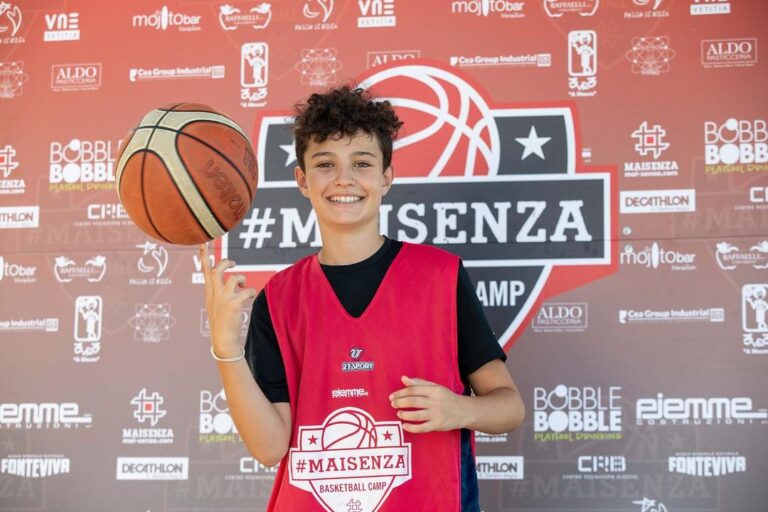 Ragazzo con canotta del camp fa girare il pallone sul dito davanti al pannello #MAISENZA