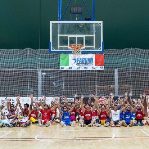 Tutti i partecipanti del camp esultano con le braccia alzate sotto il canestro in palestra